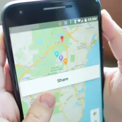 Osoba pokazuje na ekranie telefonu mapę z zaznaczoną lokalizacją i przyciskiem "Share", demonstrując, jak wysłać pinezkę.