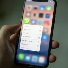 Dłoń trzyma smartfon z menu aplikacji WhatsApp. Można tu znaleźć opcję "Kopia zapasowa WhatsApp" (choć nie jest widoczna na ekranie, jest to kontekst).