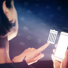 Dłoń dotyka ikony kosza na śmieci na ekranie smartfona, symbolizując czyszczenie telefonu i porządkowanie danych.