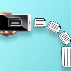 Dłoń trzyma smartfon, z którego wypadają dokumenty prosto do kosza. Tak właśnie działa opcja "gdzie jest kosz w telefonie" przy usuwaniu plików.