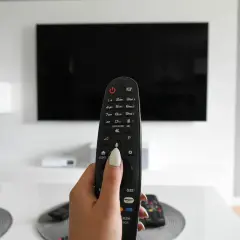 Dłoń trzymająca pilot od telewizora na tle czarnego ekranu 4K.