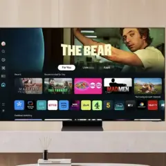 Telewizor z systemem Tizen prezentuje interfejs z filmami i serialami, w tym "The Bear". Widoczne są ikony aplikacji: Netflix, Prime Video, Disney+.