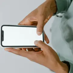 Dłonie trzymające smartfon z białym ekranem.