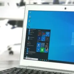 Laptop z systemem Windows 10 LTSC na biurku, w tle biuro z krzesłami.