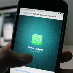 Dłoń trzyma smartfon z otwartą aplikacją **WhatsApp Business**. Na ekranie widnieje zielone logo aplikacji i jej nazwa.