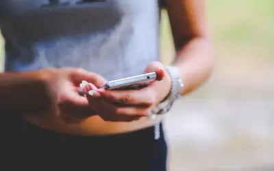 Dłonie z zadbanymi paznokciami trzymają srebrny telefon. To zrzut ekranu Samsunga, uchwycony w letnim otoczeniu.
