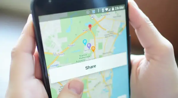 Osoba pokazuje na ekranie telefonu mapę z zaznaczoną lokalizacją i przyciskiem "Share", demonstrując, jak wysłać pinezkę.