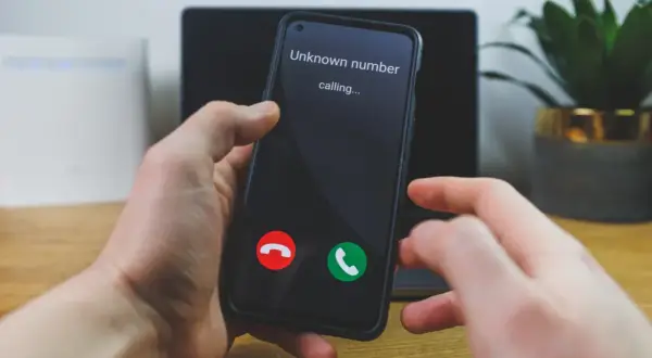 Dłoń trzyma telefon, na ekranie którego wyświetla się "Unknown number calling...". Czy to ważny numer prywatny?