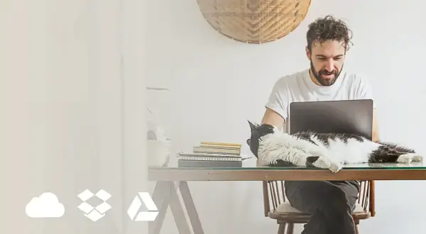 Mężczyzna pracuje przy laptopie, a kot leży na biurku. Ikony chmury, pudełka i trójkąta symbolizują online photo storage options.
