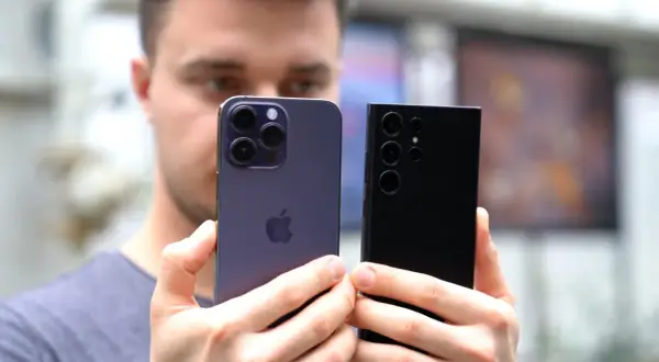 Mężczyzna porównuje iPhone'a i Samsunga, zastanawiając się, jaki telefon ma najlepszy aparat.