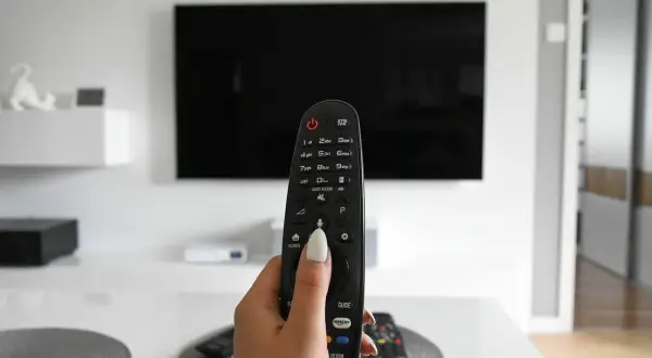 Dłoń trzymająca pilot od telewizora na tle czarnego ekranu 4K.