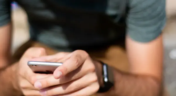 Mężczyzna z zegarkiem na ręku trzyma smartfon, przygotowując się do sparowania zegarka z telefonem.