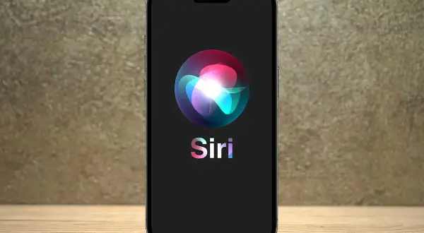 Na ekranie telefonu widnieje logo Siri, które wygląda jak kolorowa, świetlista kula.