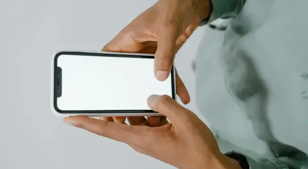 Dłonie trzymające smartfon z białym ekranem.