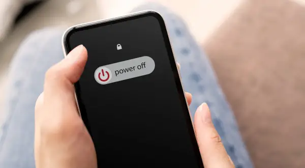 Dłoń trzyma telefon z widocznym przyciskiem "power off". Wygląda jakby telefon miał wejść w tryb awaryjny.