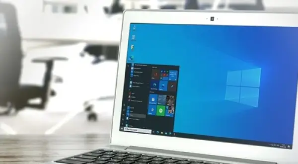 Laptop z systemem Windows 10 LTSC na biurku, w tle biuro z krzesłami.