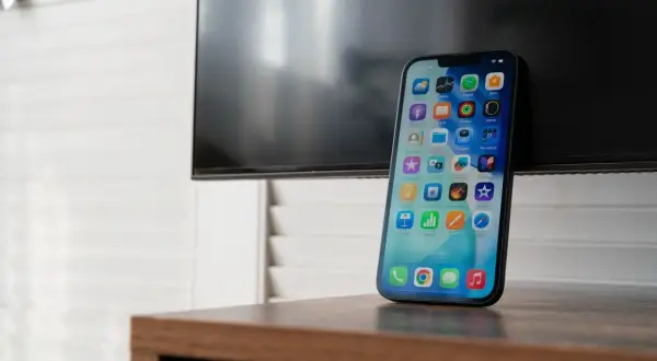 Nowy iPhone z ekranem pełnym ikon, gotowy do nagrywania rozmów. Obok czarny ekran telewizora.