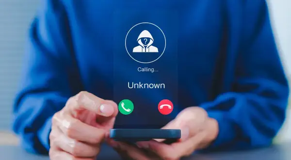 Osoba trzyma smartfon z ekranem pokazującym połączenie od nieznanego numeru. Dowiedz się, jak zablokować numer prywatny, aby uniknąć niechcianych rozmów.