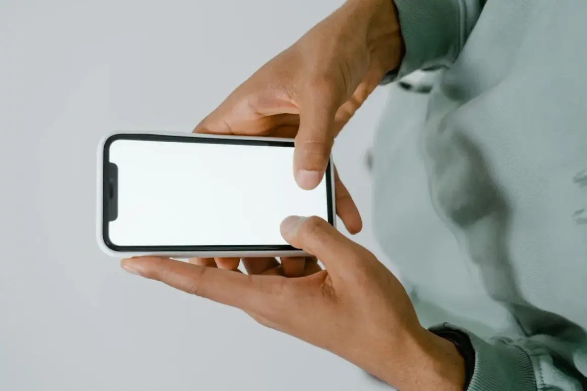 Dłonie trzymające smartfon z białym ekranem.