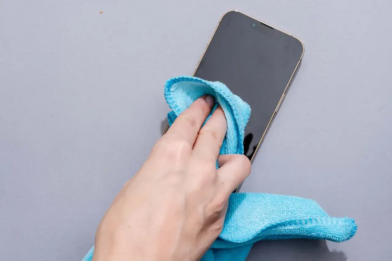 Dłoń z niebieską ściereczką czyści ekran telefonu.