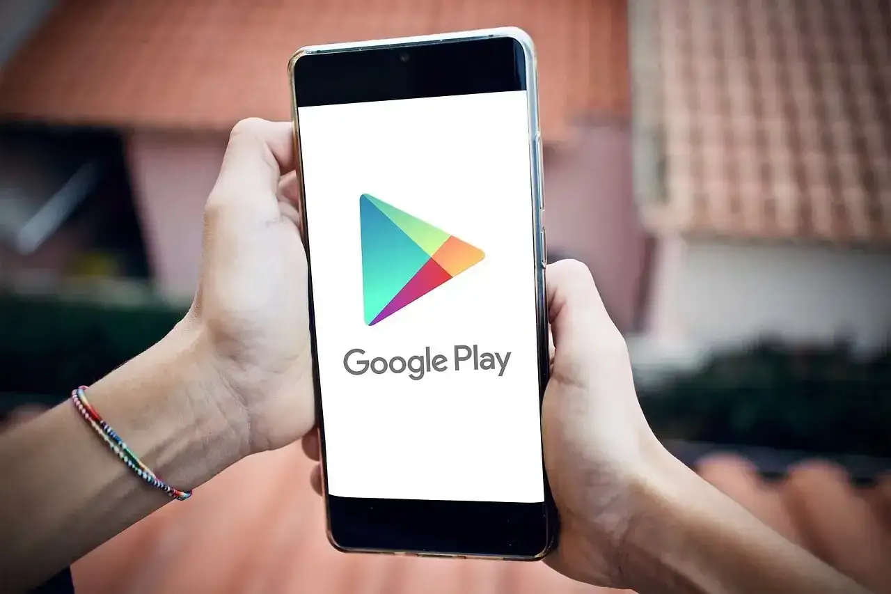 Dłonie trzymają smartfon z logo Google Play. Możesz pobrać ulubioną grę lub aplikację w formacie apk.