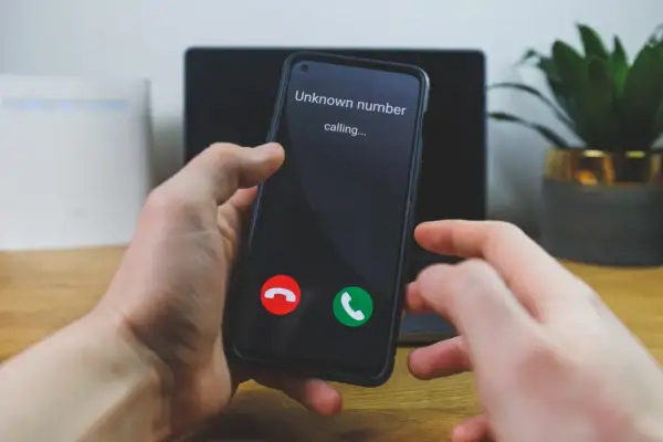 Dłoń trzyma telefon, na ekranie którego wyświetla się "Unknown number calling...". Czy to ważny numer prywatny?