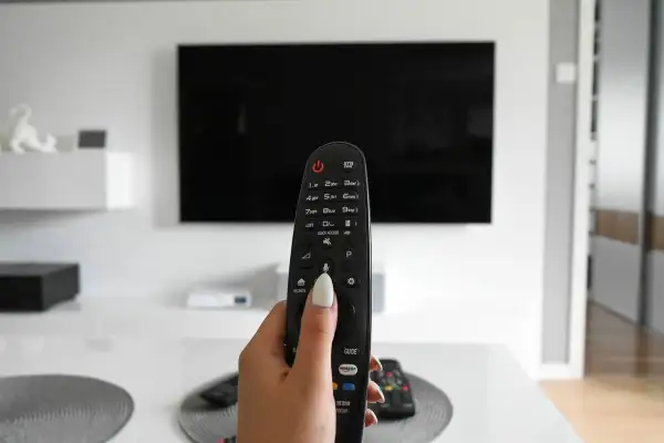Dłoń trzymająca pilot od telewizora na tle czarnego ekranu 4K.