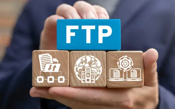 Ręce trzymają klocki symbolizujące transfer plików przez ftp: folder z ikonami pobierania/wysyłania, serwery w sieci, laptopy z dokumentami i mechanizmem.