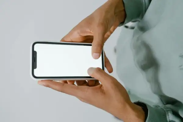 Dłonie trzymające smartfon z białym ekranem.