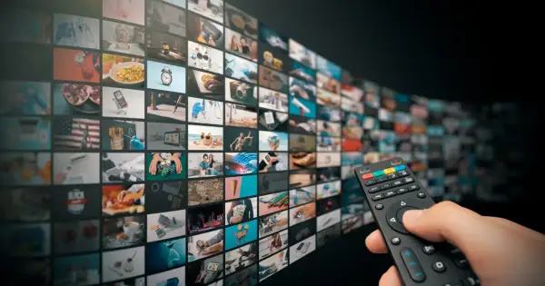 Dłoń trzymająca pilot do telewizora, wybierająca treści z ekranu z wieloma oknami, sugerującymi interaktywne funkcje HbbTV.