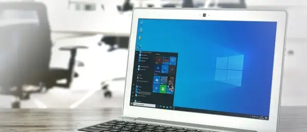 Laptop z systemem Windows 10 LTSC na biurku, w tle biuro z krzesłami.
