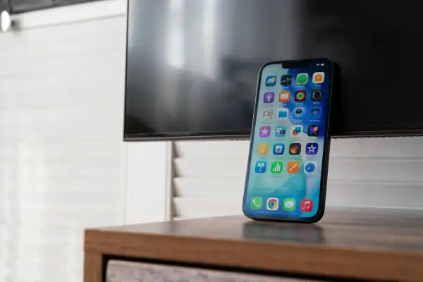 Nowy iPhone z ekranem pełnym ikon, gotowy do nagrywania rozmów. Obok czarny ekran telewizora.